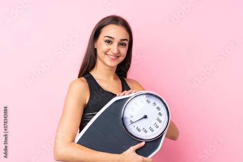 Pretty young girl with weighing machine over isolated pink background with weighing machine