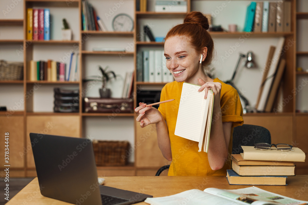 Image of girl showing exercise book while doing homework with laptop Image of girl showing exercise book while doing homework with laptop