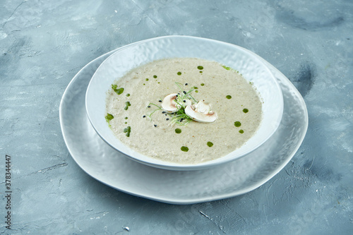 Diet mushroom cream soup with croutons with cheese in a white plate on a gray background