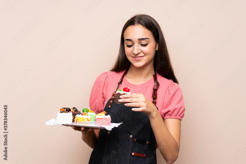 Young woman over isolated background holding mini cakes Young woman over isolated background holding mini cakes