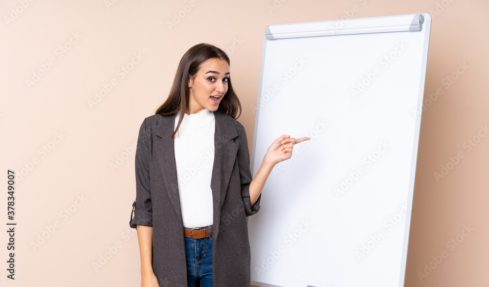 Young woman giving a presentation on white board surprised and pointing finger to the side Young woman giving a presentation on white board surprised and pointing finger to the side