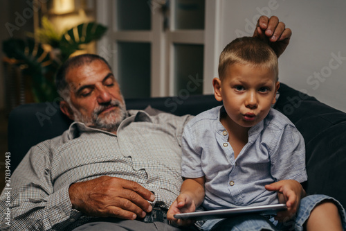 grandfather and his grandson relaxing on sofa at home using tablet computer