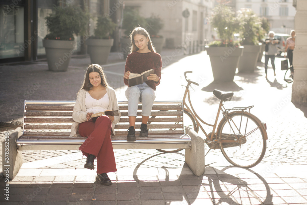 
two young girls read a book on a bench
