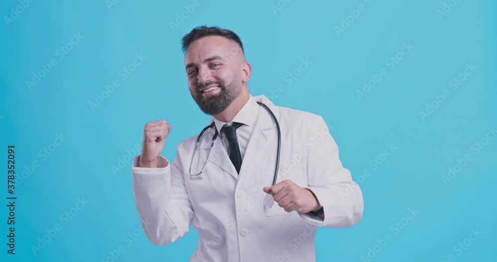 Happy mature doctor dancing, enjoying success and achievement, blue studio background Happy mature doctor dancing, enjoying success and achievement, blue studio background