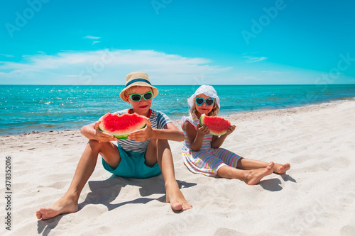 happy boy and girl eating watermelon on beach