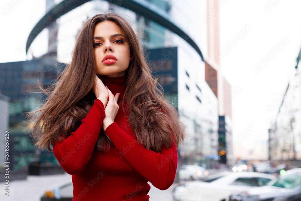 Beautiful model walking in the city. Beautiful brunette woman with big red lips, wear in jumper, hair fluttering in the wind.