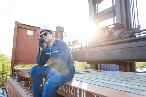 engineer using walkie-talkie in shipping yard. foreman control loading Containers box by VHF walkie-talkie radio and laptop computer in hand.