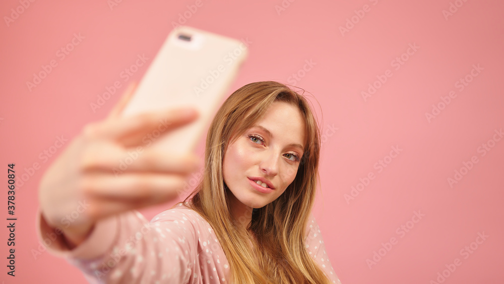 Teenage girl in pajamas taking selfies using the smartphone. Isolated on pink background. High quality photo