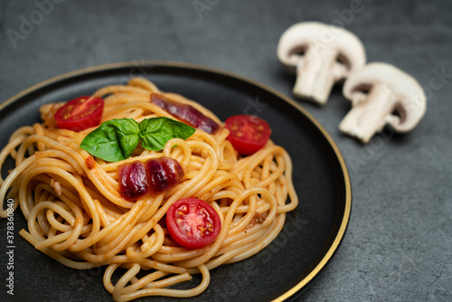 Tomato spaghetti on a black plate.A plate of spaghetti and ingredients on a dark gray cement floor