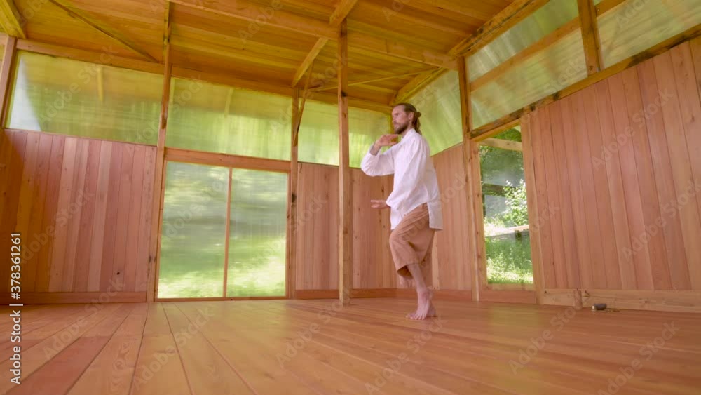 A Caucasian bearded man with long blond hair practices qigong and taichi in a wooden practice room in the summer forest. The practice of martial arts in European territories A Caucasian bearded man with long blond hair practices qigong and taichi in a wooden practice room in the summer forest. The practice of martial arts in European territories