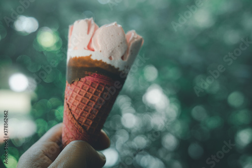 Ice cream strawberry wafer in hand against on nature blur background