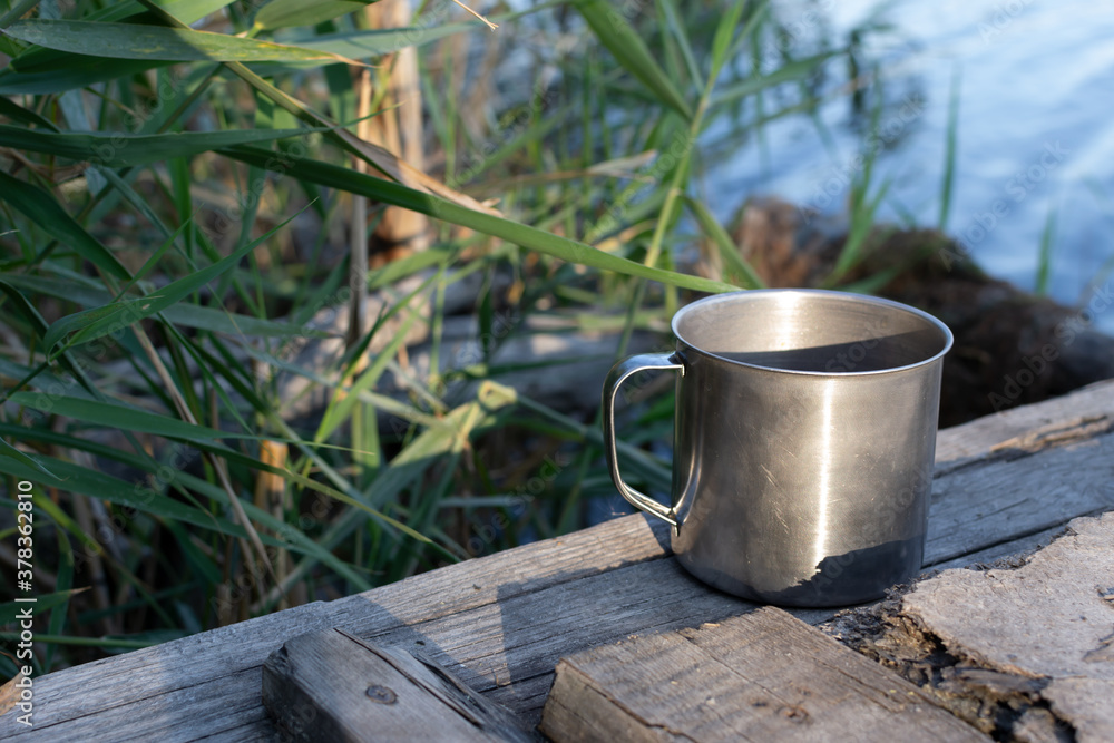 Hot tea in a metal cup on a wooden bridge over the river next to the reeds. Autumn weekend. Selective focus. Horizontal orientation. Hot tea in a metal cup on a wooden bridge over the river next to the reeds. Autumn weekend. Selective focus. Horizontal orientation.