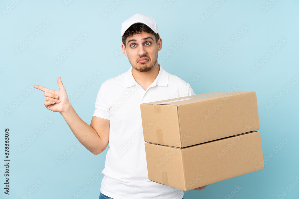 Delivery caucasian man isolated on blue background pointing to the laterals having doubts Delivery caucasian man isolated on blue background pointing to the laterals having doubts