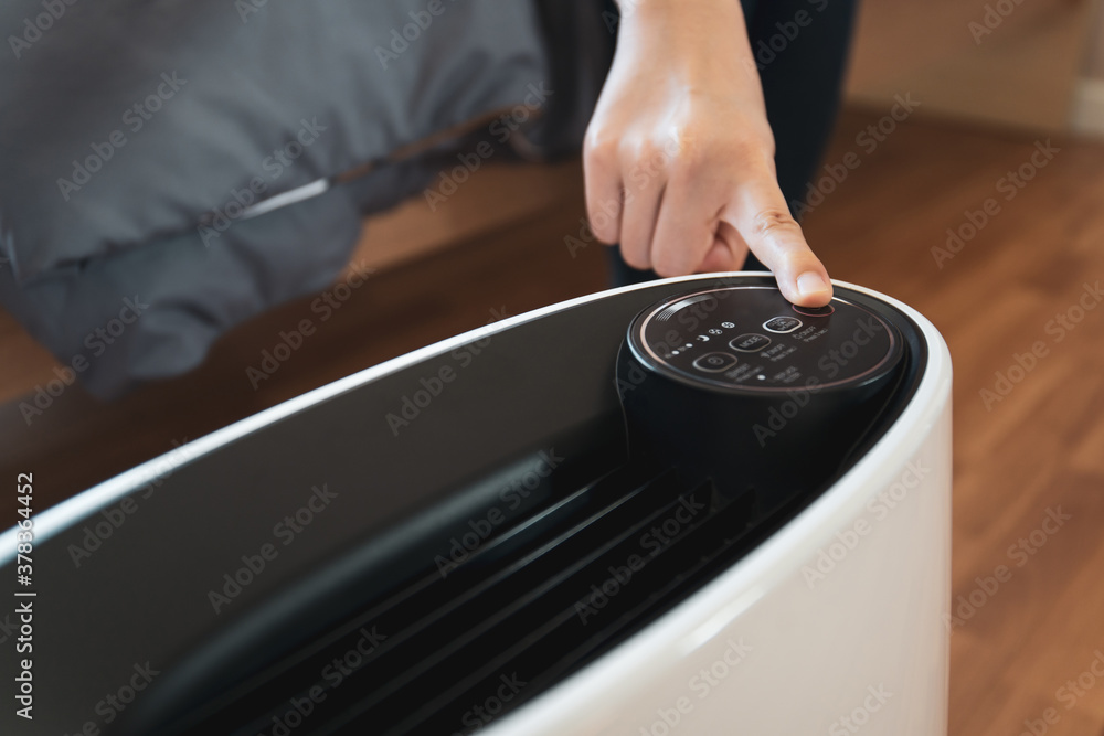 Asian sleepy woman trying to press a button on the portable air purifier machine in a bedroom. Asian sleepy woman trying to press a button on the portable air purifier machine in a bedroom.