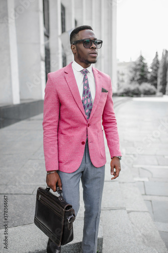 Men's Fashion. A stylish young man dressed in business style in a pink jacket poses on the street of a high-rise building. 