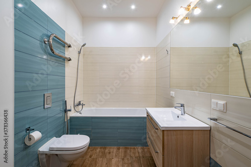 Contemporary interior of luxury bathroom in apartment. Mirror and sink with wooden drawers. Bath and toilet.