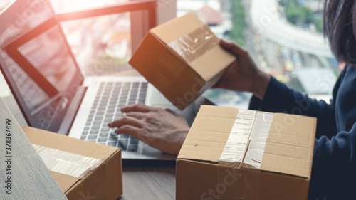 Woman hands holding a parcel box and using a laptop for business at home and laptop on background with copy space. Business start up SME concept. © PHICHCHA