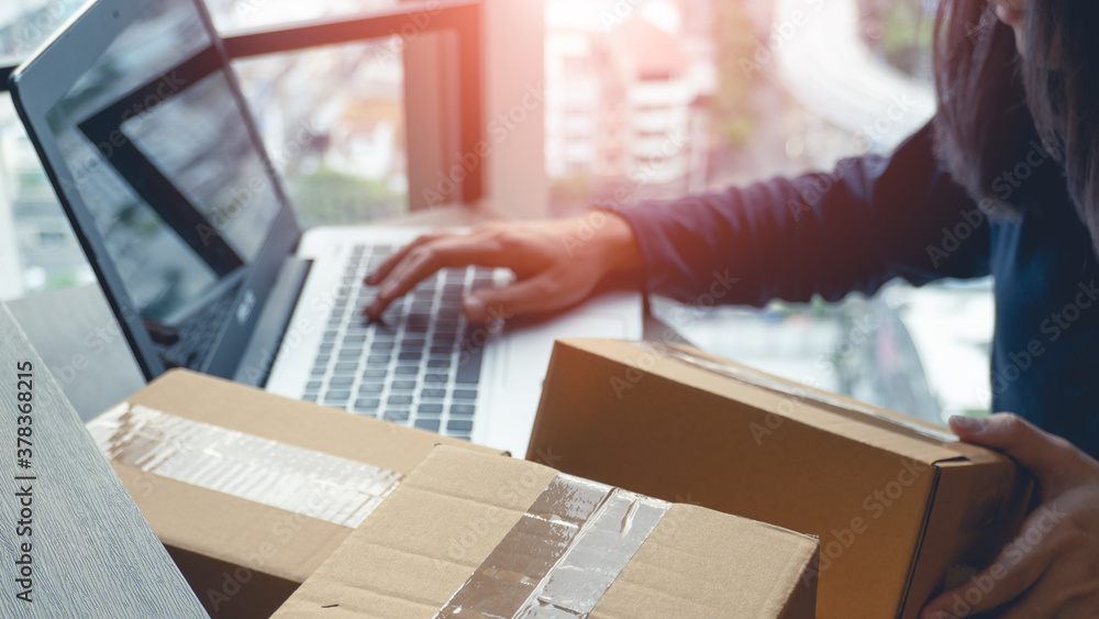 Woman hands holding a parcel box and using a laptop for business at home and laptop on background with copy space. Business start up SME concept. Woman hands holding a parcel box and using a laptop for business at home and laptop on background with copy space. Business start up SME concept.
