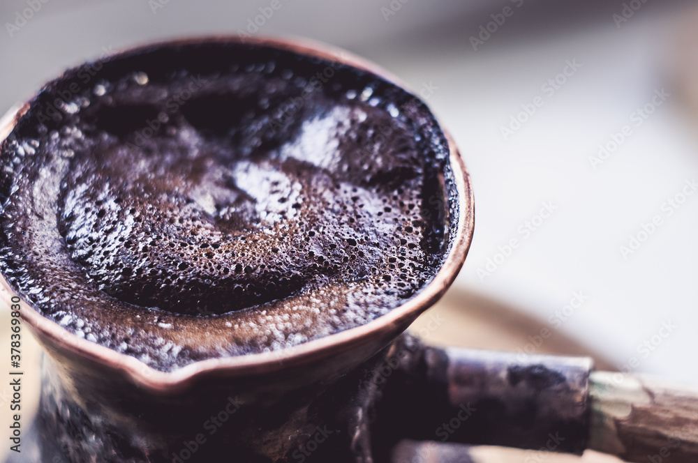 Fototapeta premium Natural coffee with thick foam, brewed in a copper cezve in the classical way, on a wooden background, macro photo.