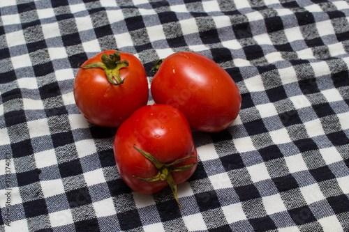 juicy red tomatoes in table cloth . caro background 