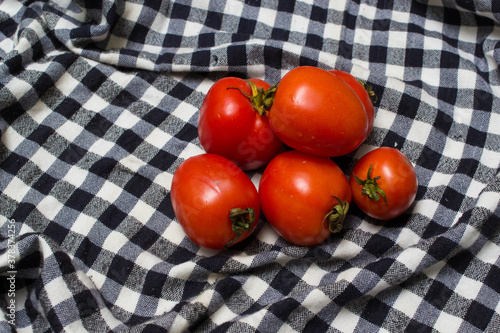 juicy red tomatoes in table cloth . caro background 