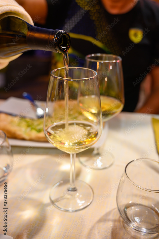 Fototapeta premium Pouring in glass cold dry white wine in outdoor cafe at night in Italy