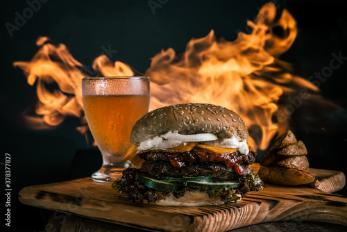 Close-up of a hamburger with french fries and a glass of beer with fire flames. Grilled