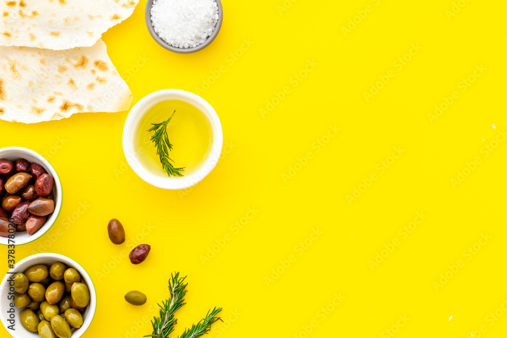 Top view of olives, olive oil, bread on yellow table top view copy space