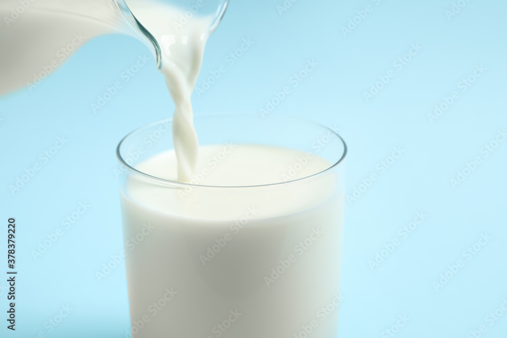 Pouring milk into glass on light blue background, closeup Pouring milk into glass on light blue background, closeup