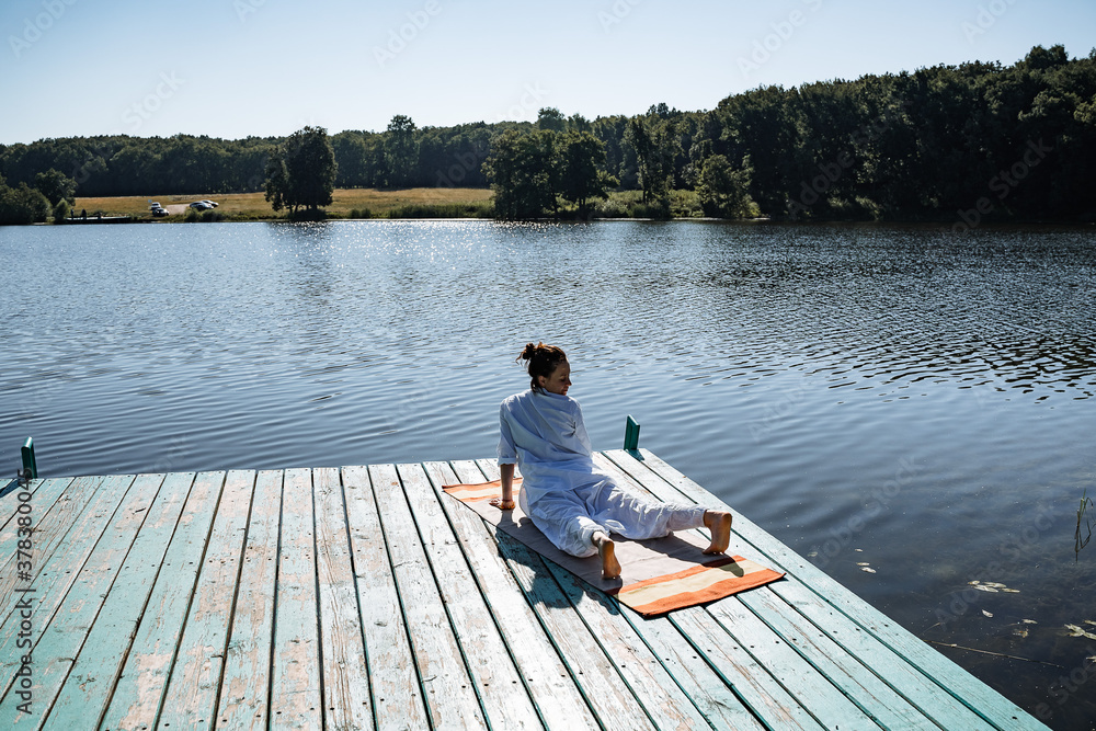 a young girl in white clothes does yoga on a pier on a summer Sunny day, yoga asana pose, morning gymnastics, outdoor fitness, sun salute complex
