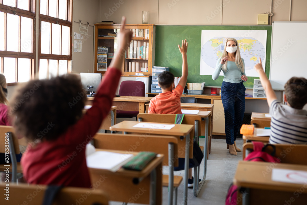 Group of kids raising their hands in the class at school