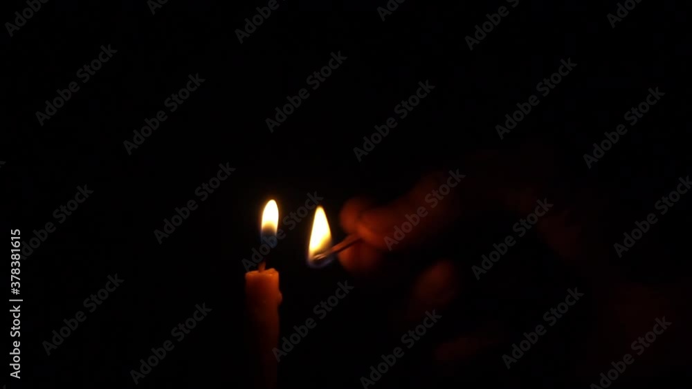 A man hand lit a yellow candle using a matchstick and a close-up. Religion concept A man hand lit a yellow candle using a matchstick and a close-up. Religion concept