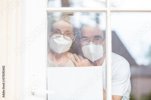 Elderly couple wearing protective face masks watch through their home window during the coronavirus epidemic and shows empty page