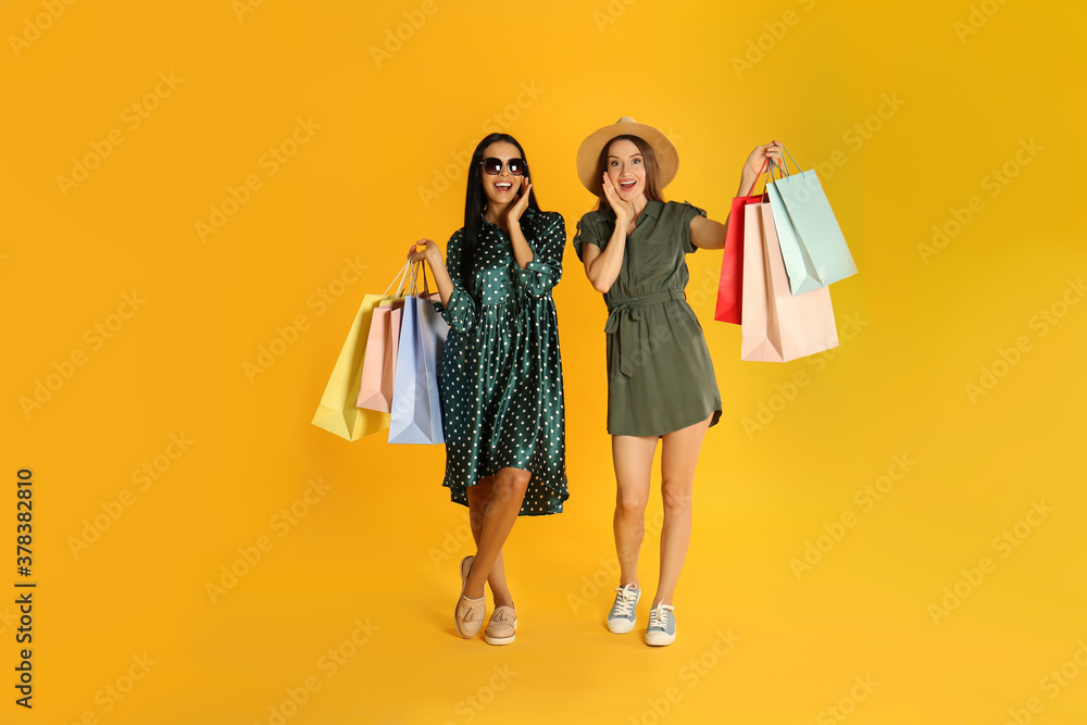 Beautiful young women with paper shopping bags on yellow background
