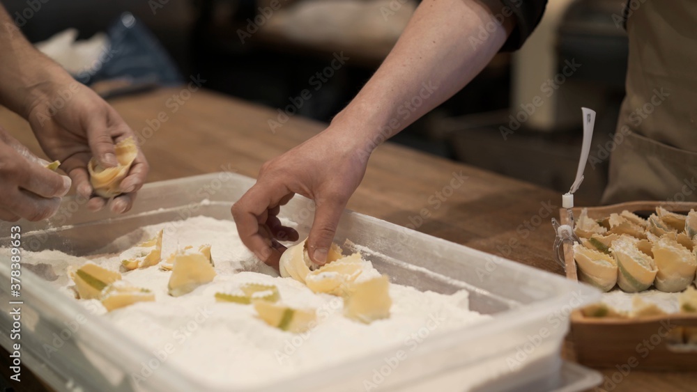 Male hands in flour on several tortellini in the tray with flour. Preparation of italian food at the restaurant kitchen, cooking italian tortellini