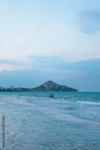 The waves hit the coast in the evening. A woman and a man were Hands in hand together in the middle of ocean. The background has an island with a clear sky in the soft. There is a copy space. © Pang wrp