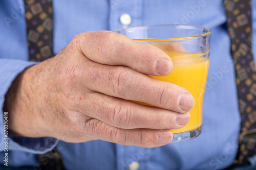 the rough hands of an elderly male holding a glass of orange juice