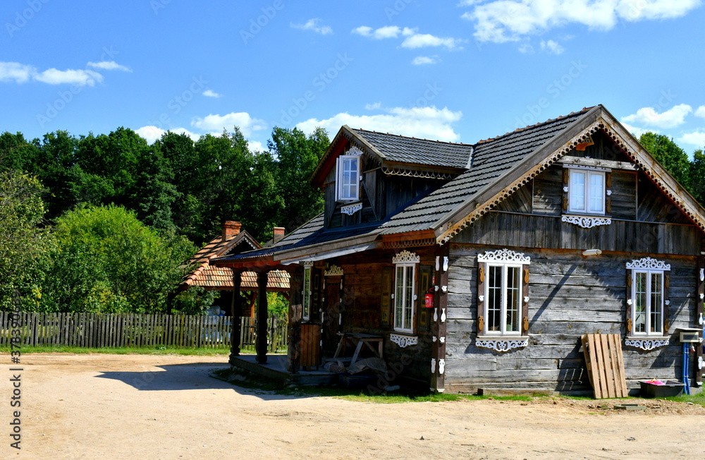 View of a small decorative old shack or hut with wooden door and window frames and walls made out of planks and logs located on a paddock next to a dense orchard or forest seen in Poland