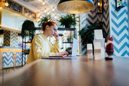 Intelligent female entrepreneur checking delivery information on provide website during work day in own cafeteria with loft design, skilled freelancer watching online webinar via lptop device photo