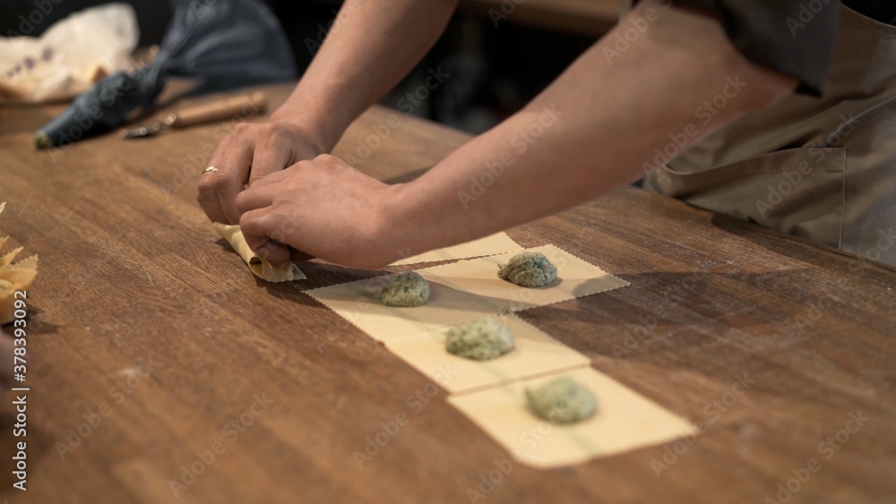 Cook preparing ravioli, rolling dough with stuffing on wooden kitchen table. Male hands cooking italian food, handmade ravioli at the restaurant kitchen