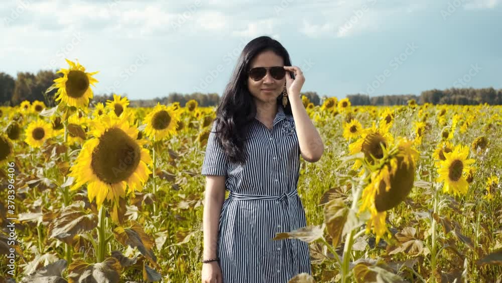 Portrait of girl wearing sunglasses, standing in sunflower field among flowers Portrait of girl wearing sunglasses, standing in sunflower field among flowers