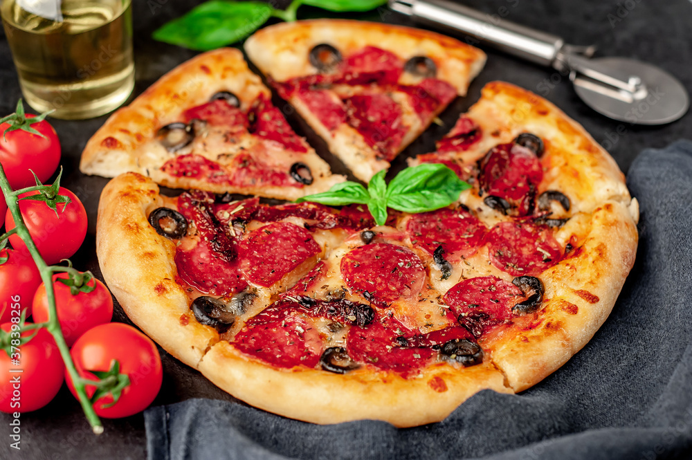 Mediterranean pizza with salami sausages, mozzarella, olives, Provencal herbs, signature tomato sauce on a stone background