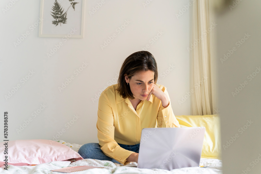 Woman using laptop while sitting on bed at home Woman using laptop while sitting on bed at home