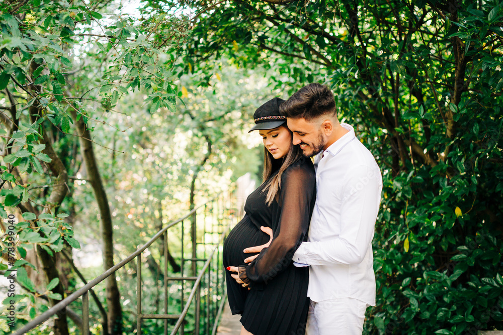 Smiling man embracing and touching belly of woman while standing in park Smiling man embracing and touching belly of woman while standing in park