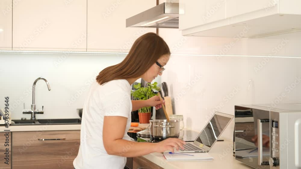 A Woman Works with Laptop on a Kitchen and Cooking same Time, Home Office A Woman Works with Laptop on a Kitchen and Cooking same Time, Home Office
