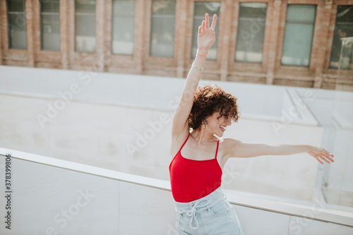 Cheerful woman with arms raised dancing by retaining wall in city