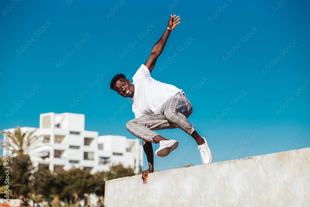 African man jumping over retaining wall against clear blue sky during sunny day African man jumping over retaining wall against clear blue sky during sunny day