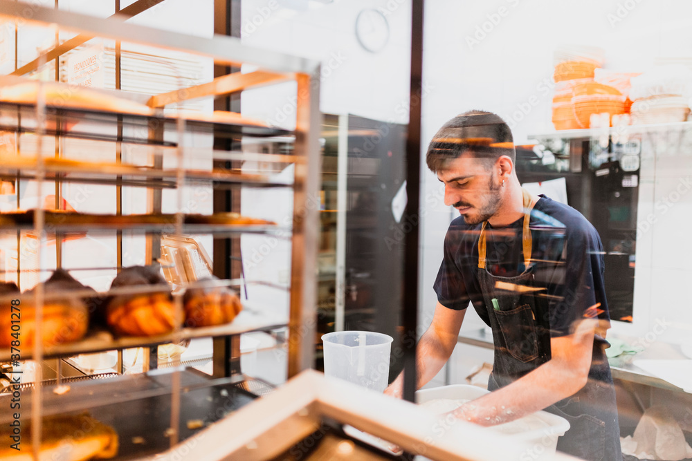 Young baker working at bakery seen through glass window Young baker working at bakery seen through glass window