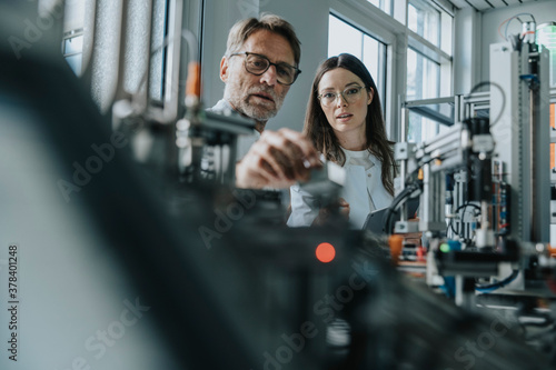 Male scientist with young woman examining machinery in laboratory photo