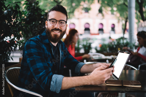 Positive man with smartphone and laptop in cafe